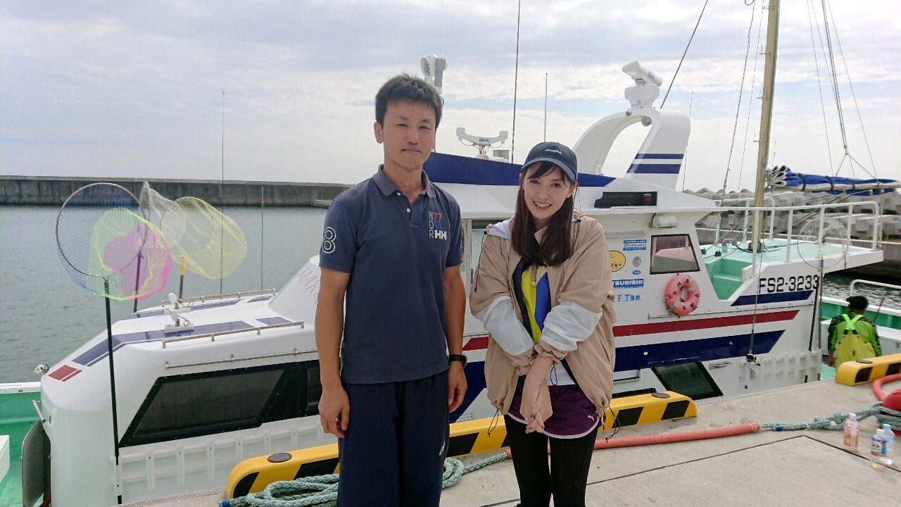 停泊している遊漁船「長栄丸」を背景に、男性漁師の石井さんとパーソナリティの高橋万里恵さんが2人並んで立っている写真