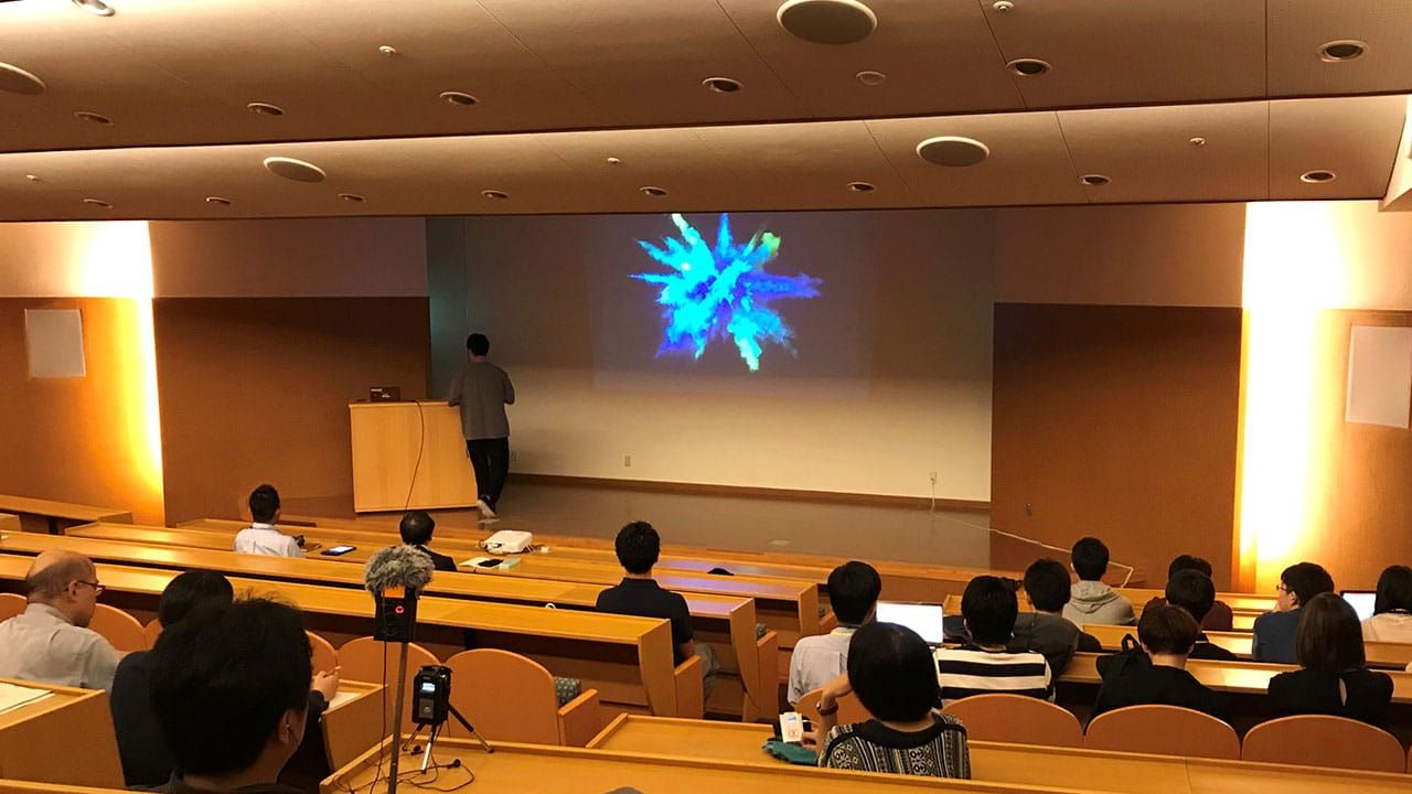 多数の聴衆を前に、ステージ上で講師がワークショップを行っている様子