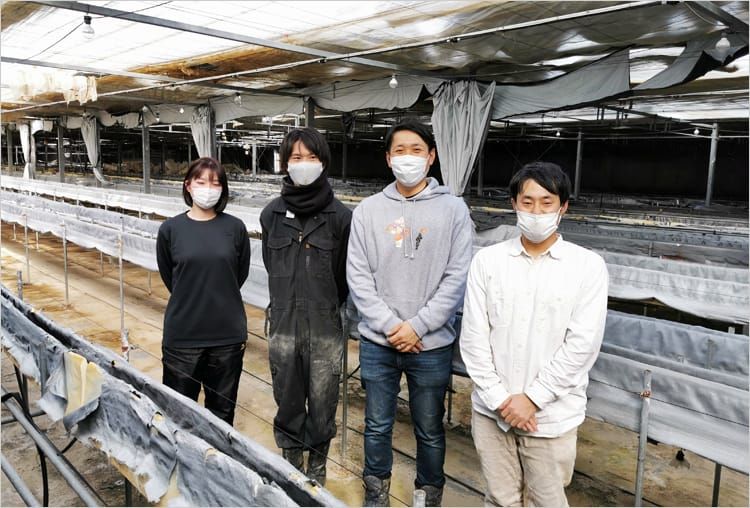 ビニールハウスの中で農業体験に訪れている大学生らと谷口さんがにこやかな笑顔を浮かべ並んでいる写真