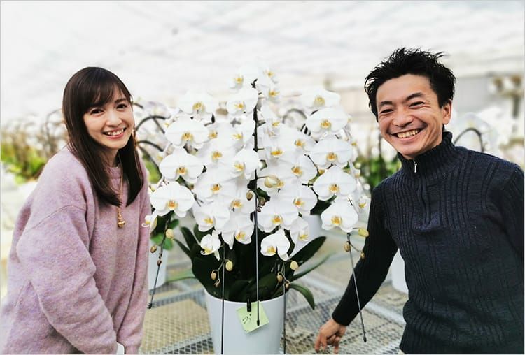 大きな白色の胡蝶蘭を挟むように並び、満面の笑みを浮かべる高橋万里恵さんと杉下博澄さんの写真