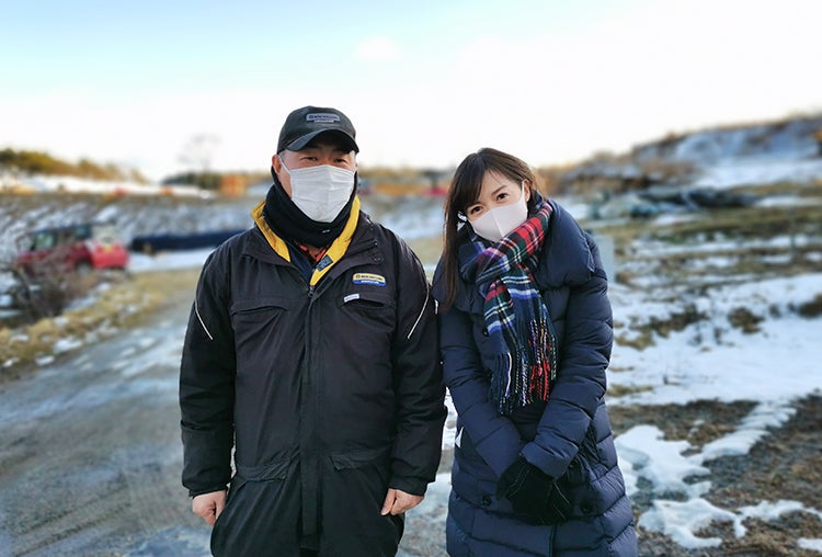 まだ雪が残る屋外で、佐久間哲次さんと高橋万里恵さんが並んで笑みを浮かべている写真