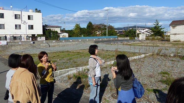 ツアー参加者らが解体され更地となった住宅跡地に立ち、小林奈保子さんの話に耳を傾けている様子