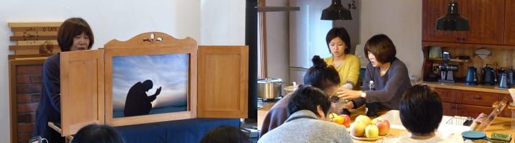 カフェオーナーの岡洋子さんが、実際の写真を用いた紙芝居を朗読している写真と、果物を持ち説明をしている岡洋子さんとその説明に耳を傾けるツアー参加者らの様子