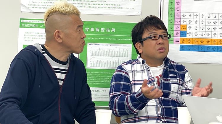 教室で天野ひろゆきさんが手振りを交えながら発言し、隣でウド鈴木さんがその話に耳を傾けている様子