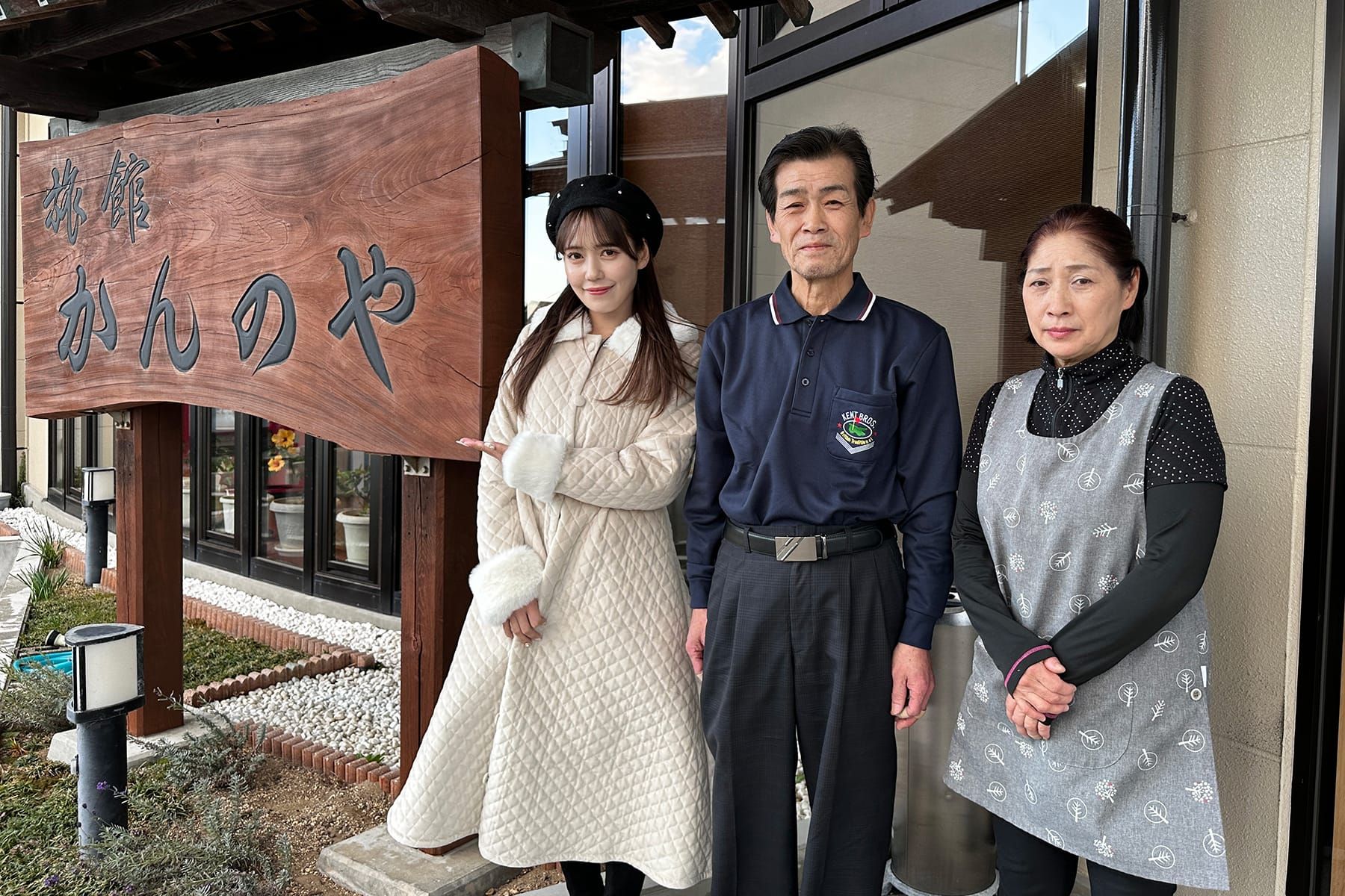 旅館かんのやの看板の前での諸橋沙夏さんと管野さん夫婦の集合写真