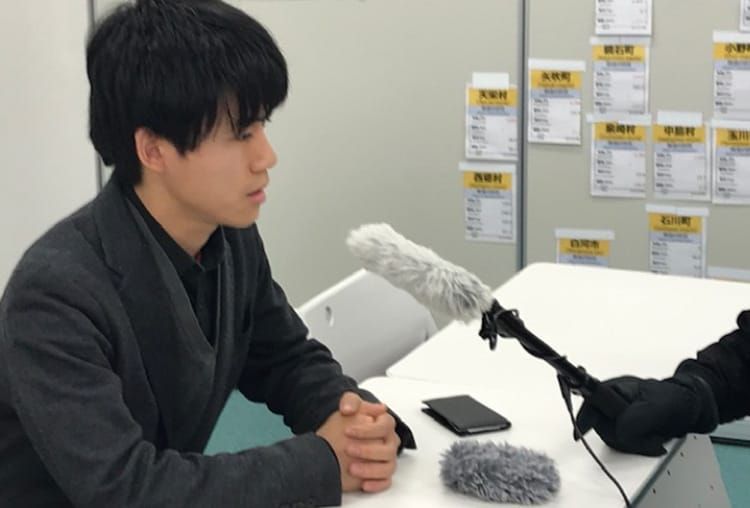 江原義哉先生がマイクの前でインタビューに答える様子の写真