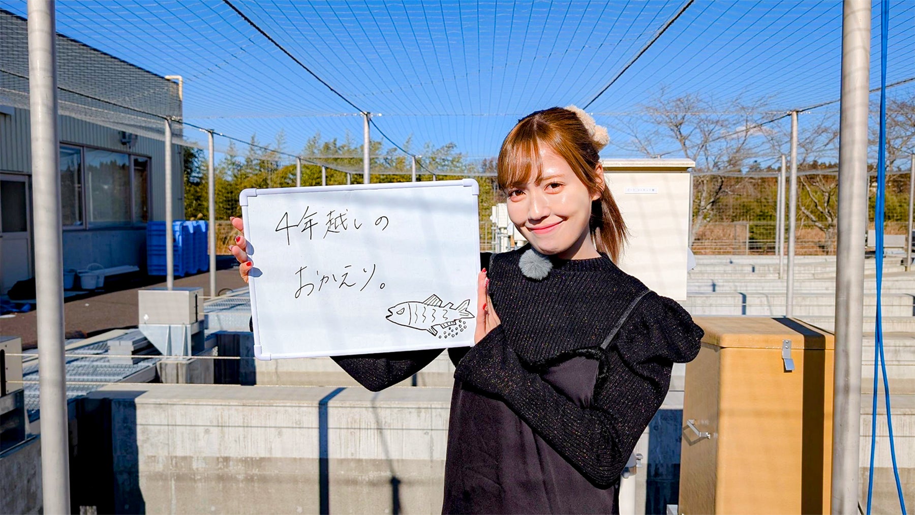 サケの絵と共に「4年越しのおかえり。」と書かれたホワイトボードを掲げる諸橋沙夏さんの写真